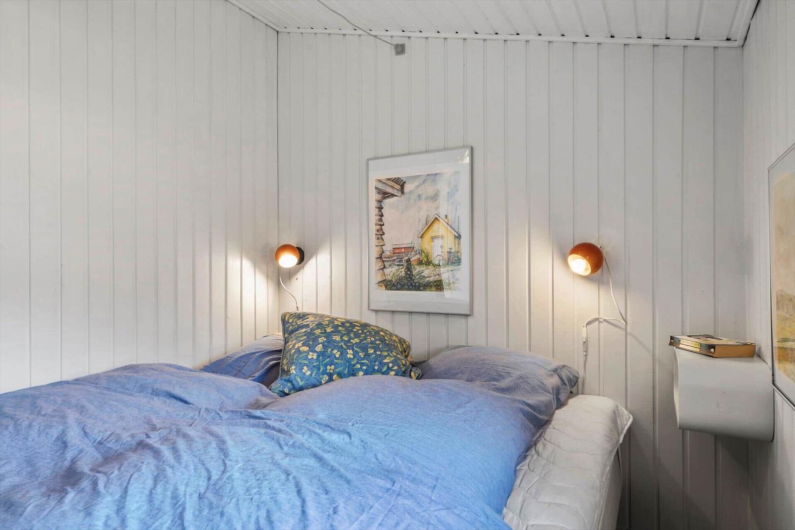 Schlafzimmer mit Bett, Wandlampen und Bild an der Wand.