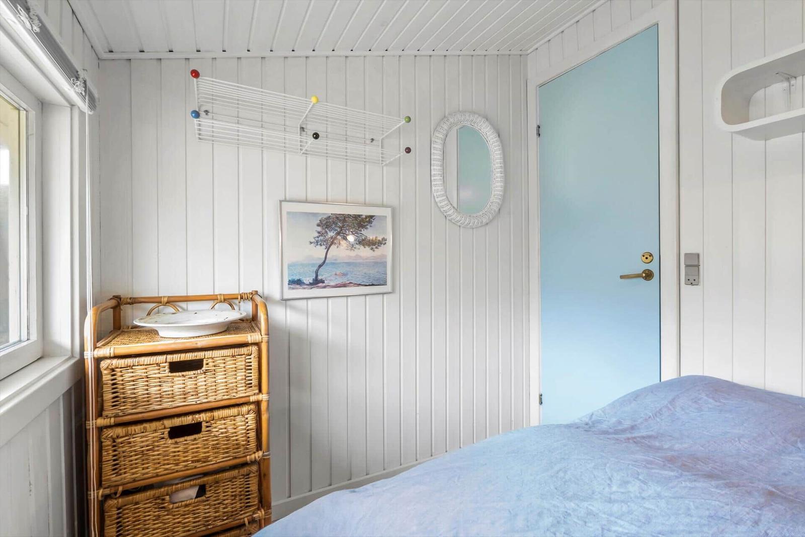 Schlafzimmer mit blauer Tür, Bett und Rattan-Schrank an der Wand.