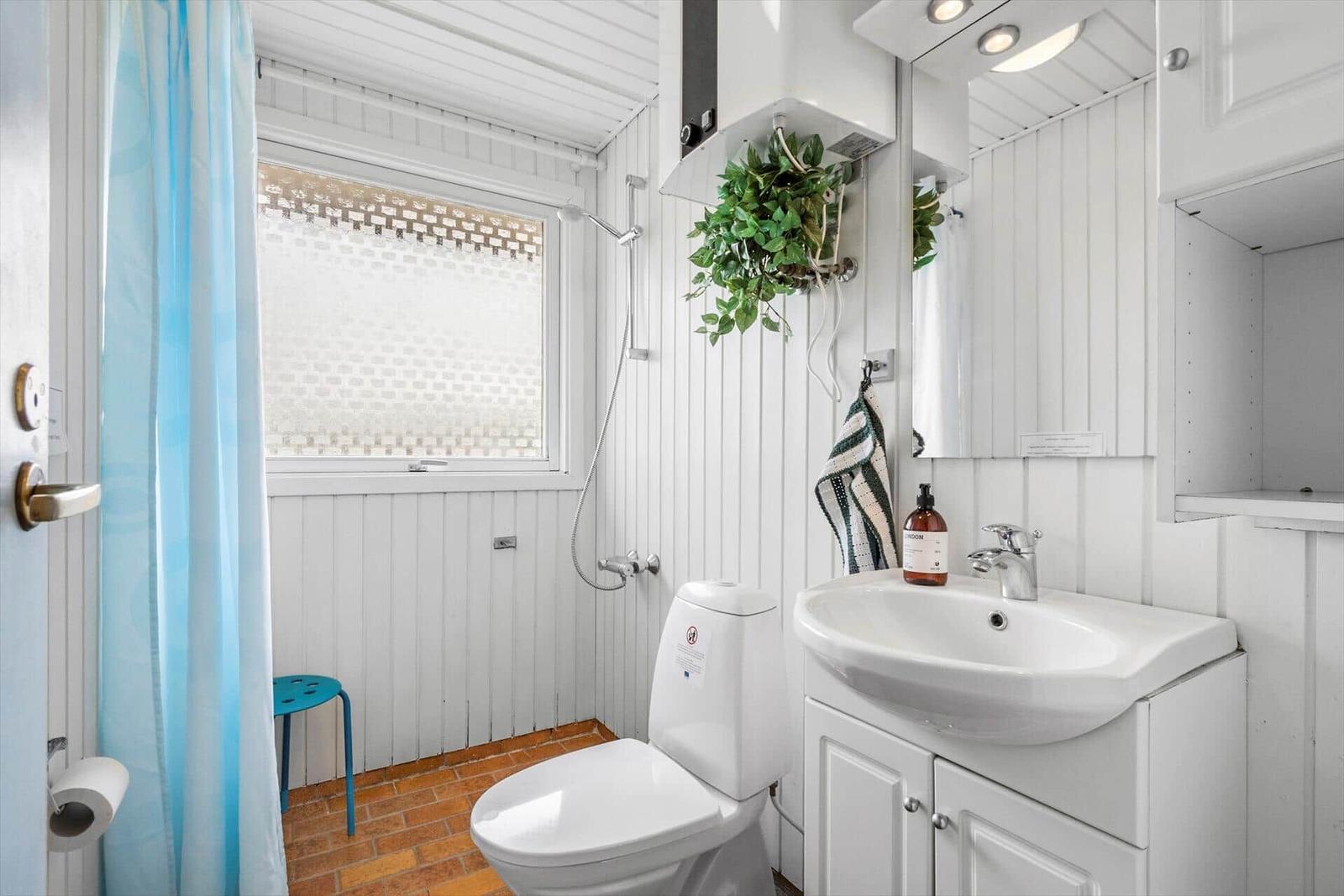 Badezimmer mit Toilette, Waschbecken und Dusche. Weiße Holzwände und brauner Boden.