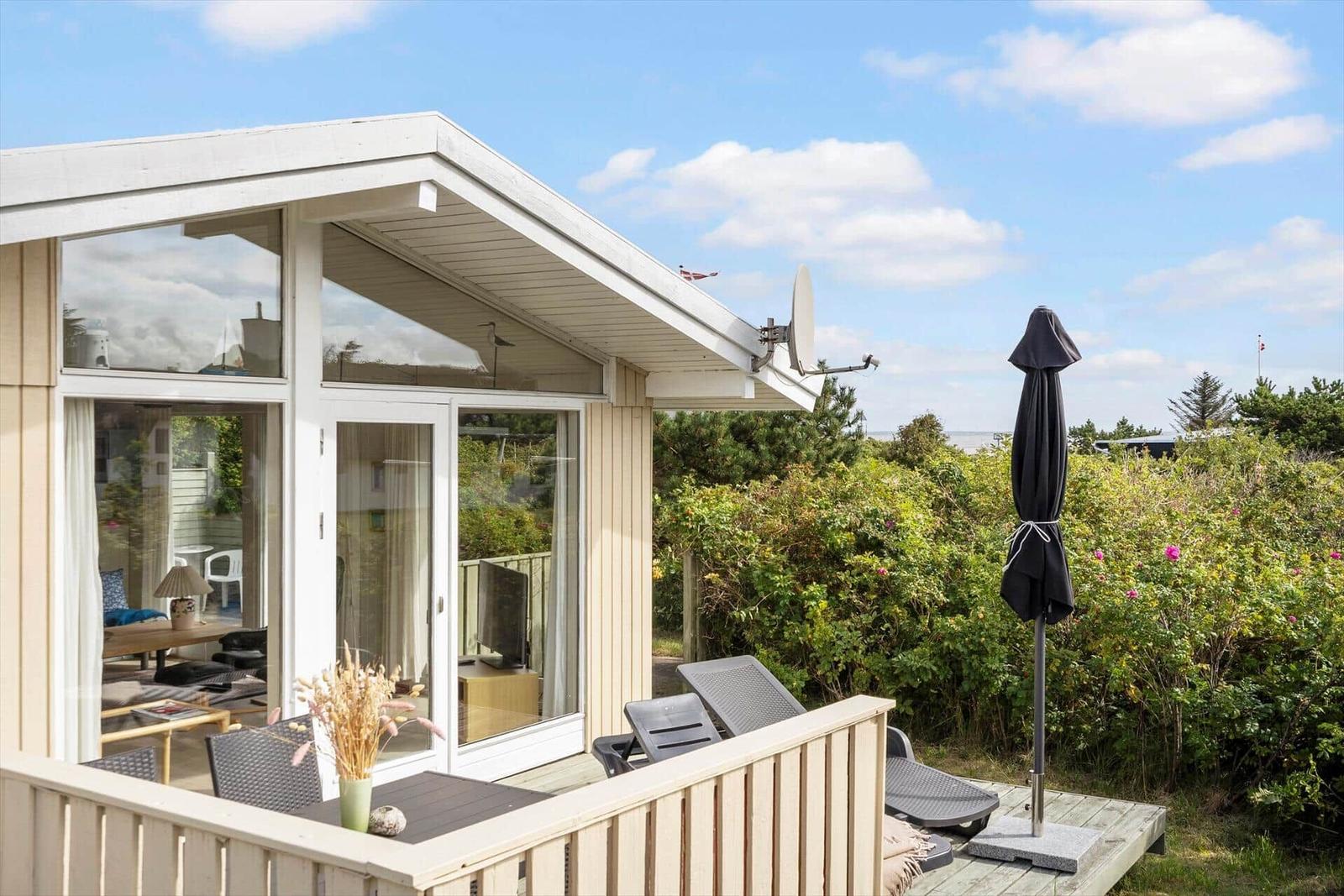 Terrasse mit Liegestühlen und Sonnenschirm neben einem Haus mit Glasfront.