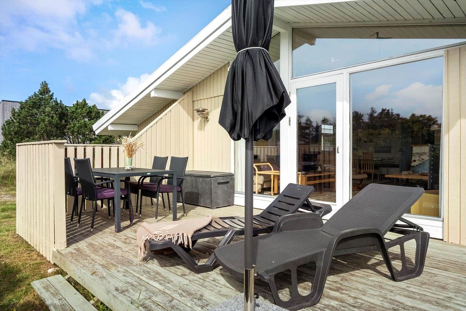 Terrasse mit Loungemöbeln, Tisch und Stühlen. Glasfront zum Innenraum. Himmel mit Wolken.