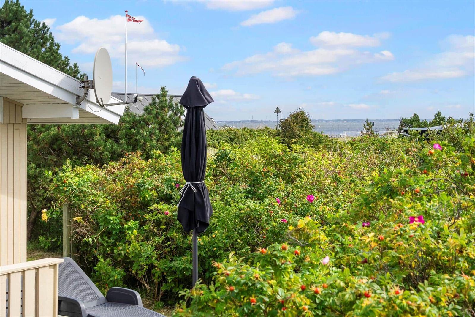 Terrasse mit Sonnenschirm und Blick auf grüne Hecken und Meer.