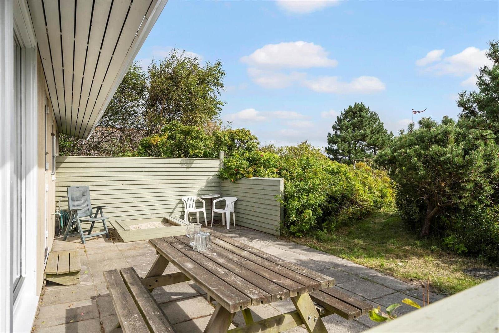 Terrasse mit Picknicktisch, Gartenmöbeln und grüner Umgebung.