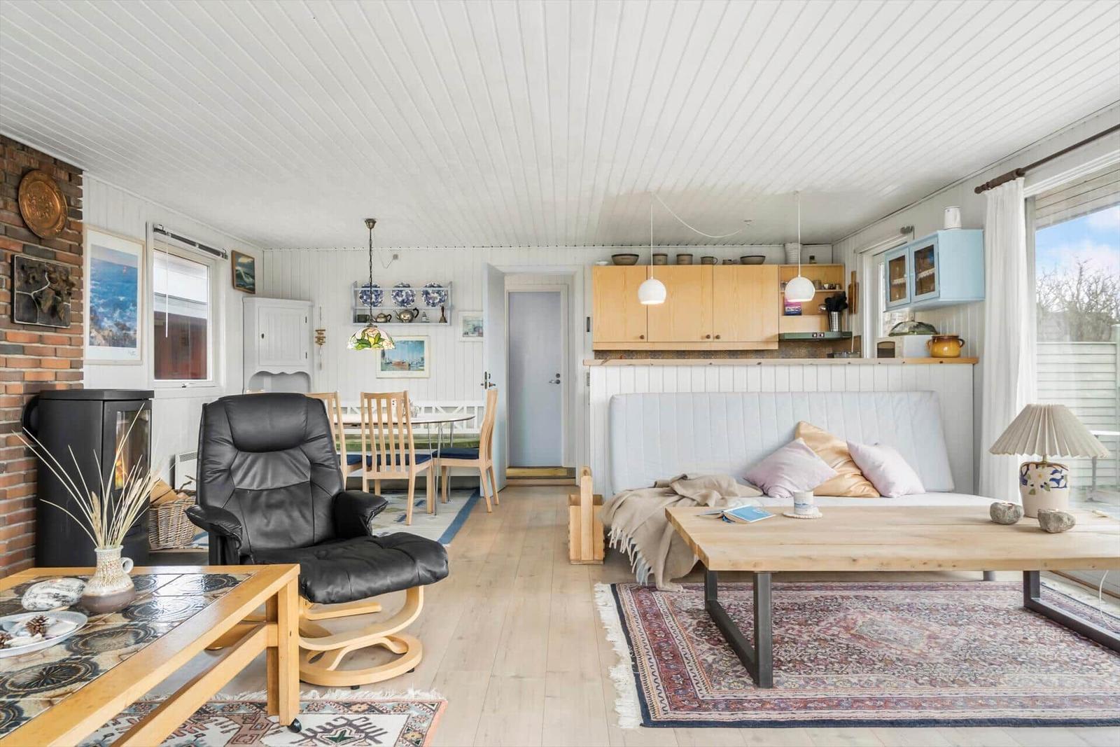 Wohnzimmer mit Sofa, Esstisch und Küchenbereich. Holzfußboden und weiße Wände.