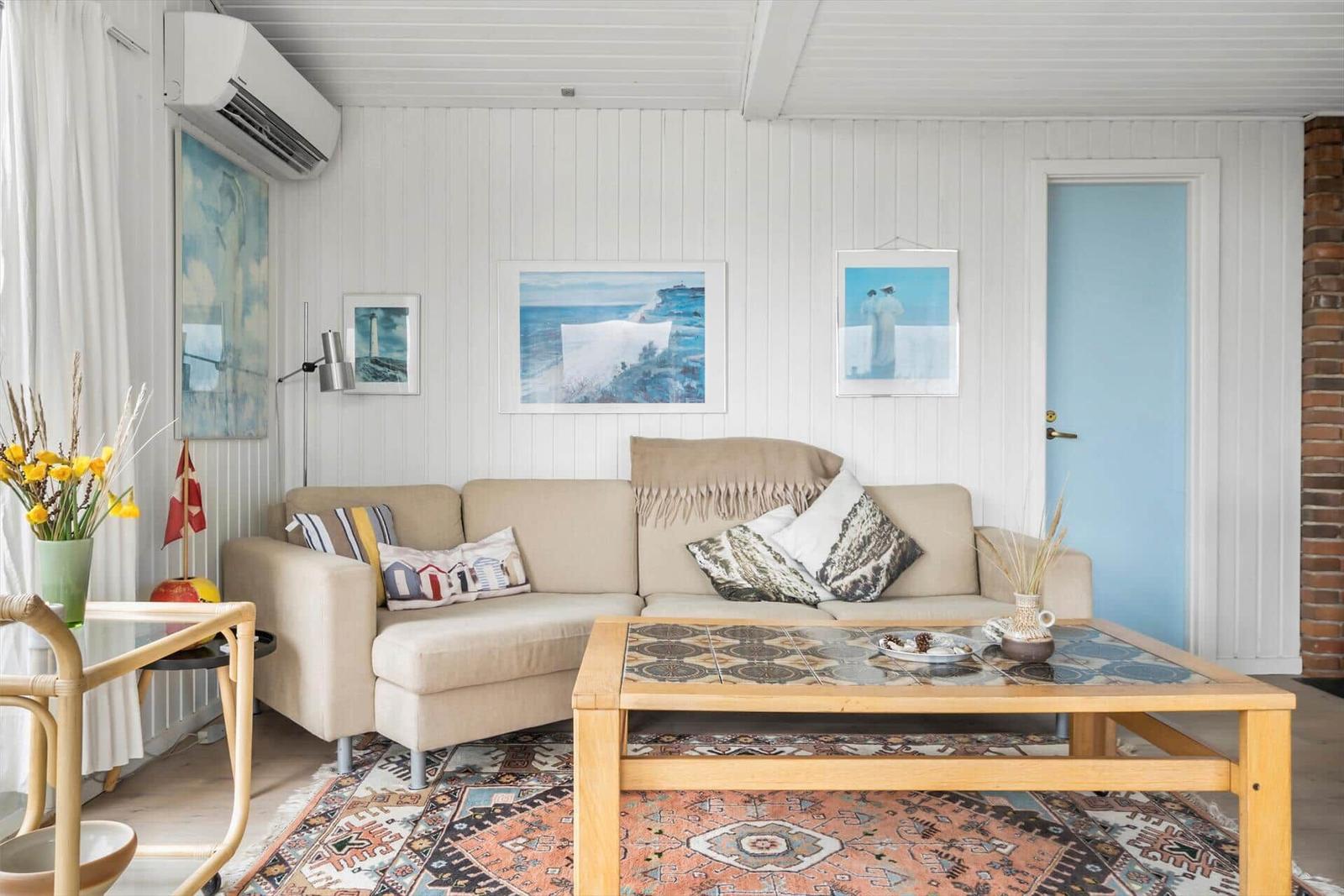 Wohnzimmer mit Sofa, Couchtisch und Wandbildern an weißen Holzwänden.