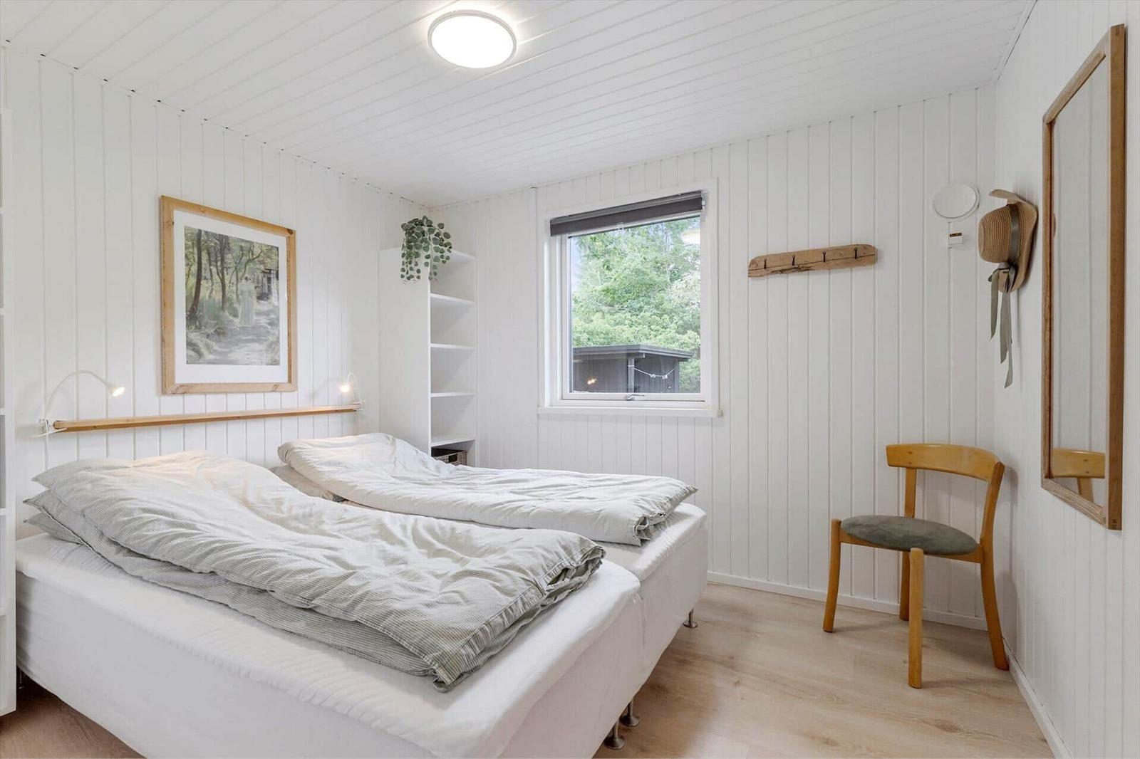 Schlafzimmer mit Bett, Stuhl, Spiegel und Fenster mit Blick auf Wald.