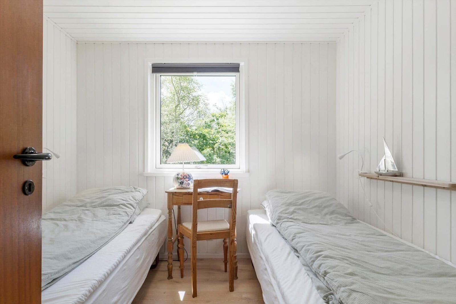 Zwei Einzelbetten, ein Schreibtisch mit Stuhl und ein Fenster mit Blick auf Bäume.