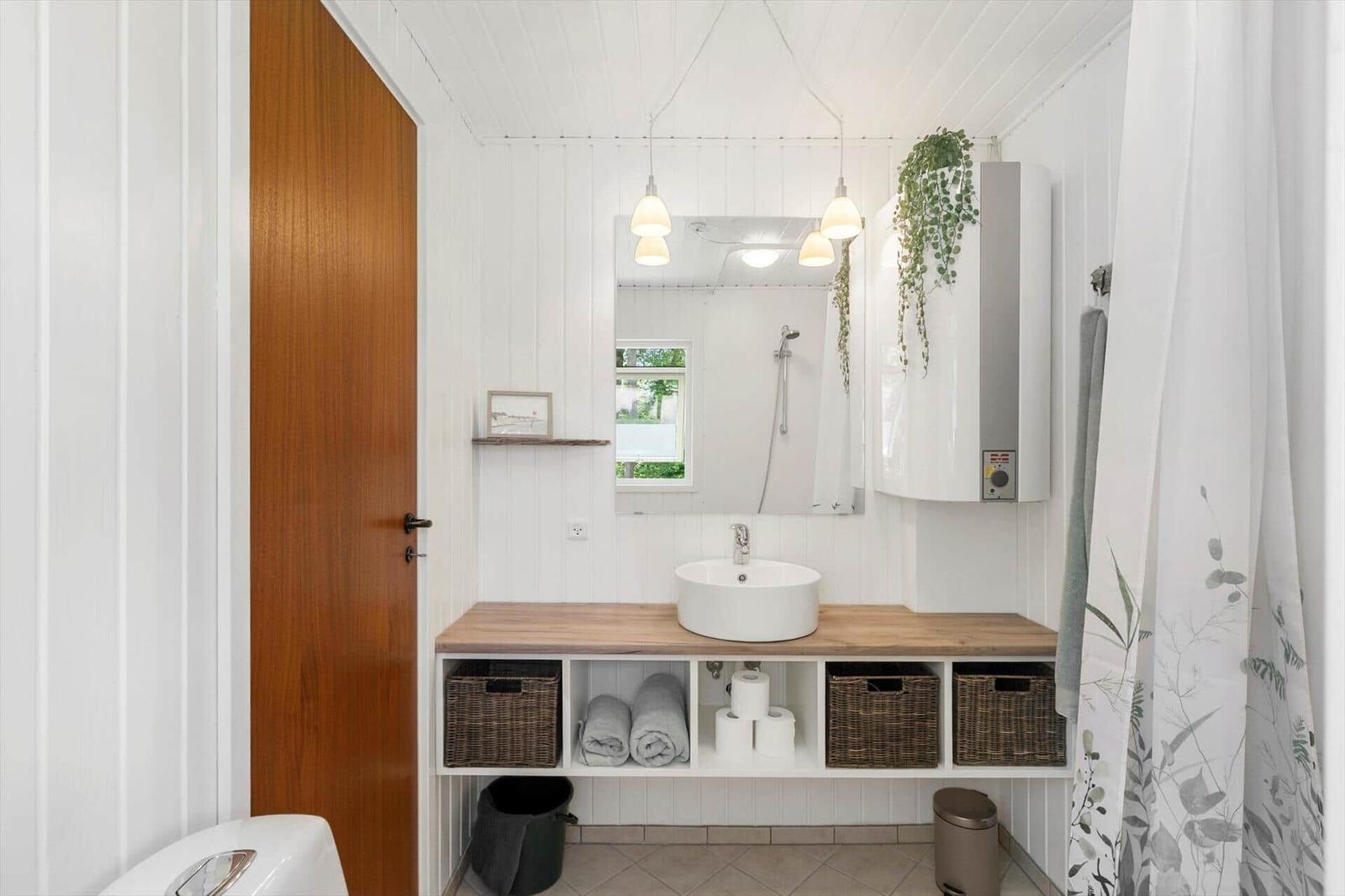 Badezimmer mit Waschtisch, Spiegel und Dusche. Holzunterschrank und Pflanze.