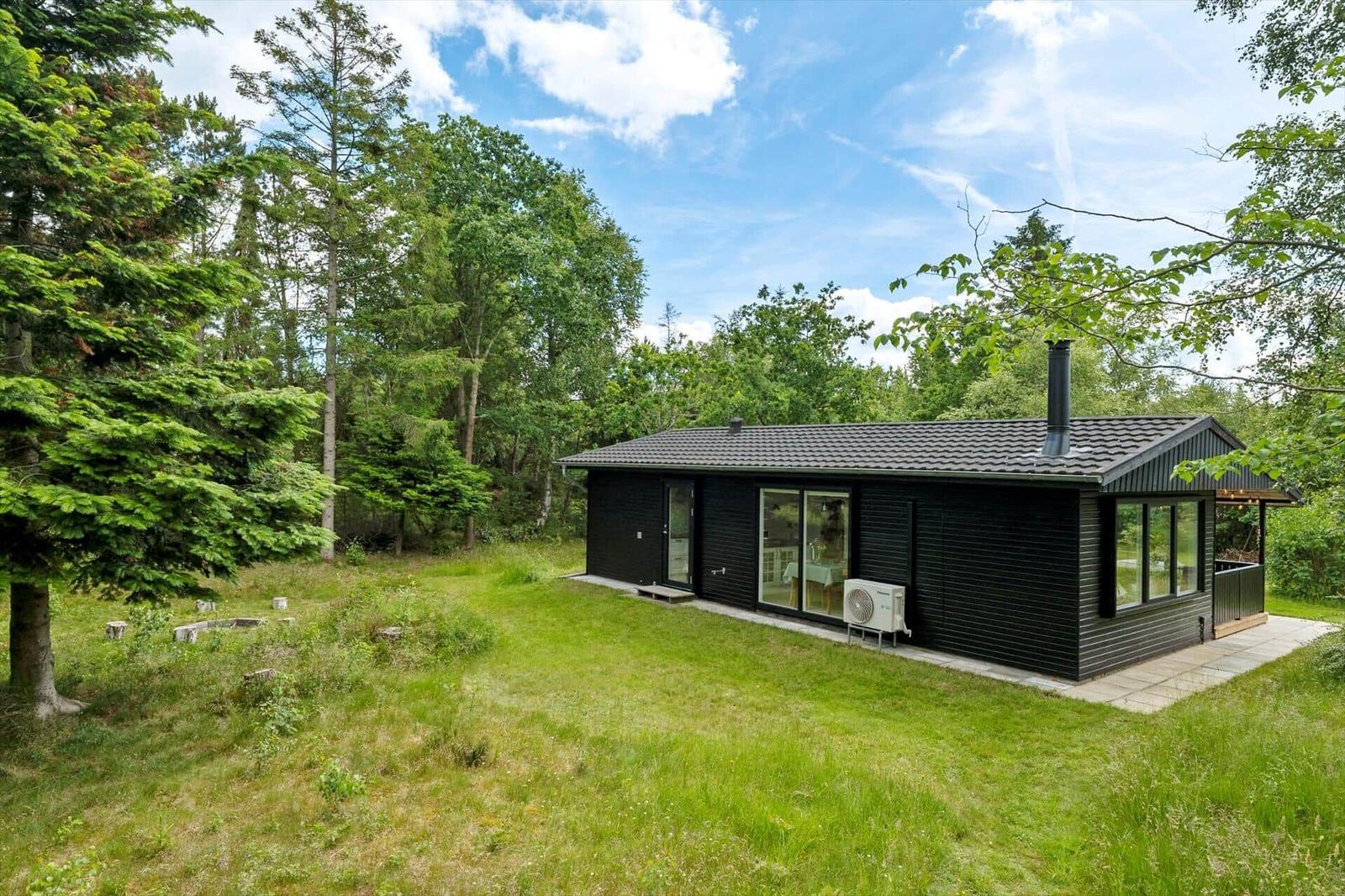 Schwarzes Holzhaus mit großem Grundstück und Wald im Hintergrund.