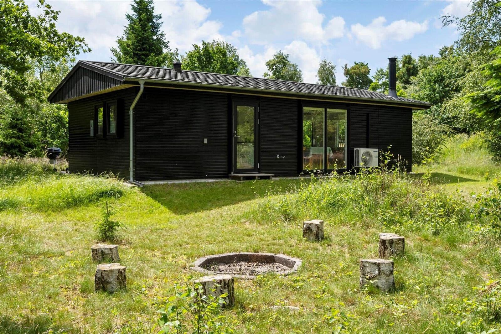 Schwarzes Holzhaus mit Grill und Feuerstelle im Gras