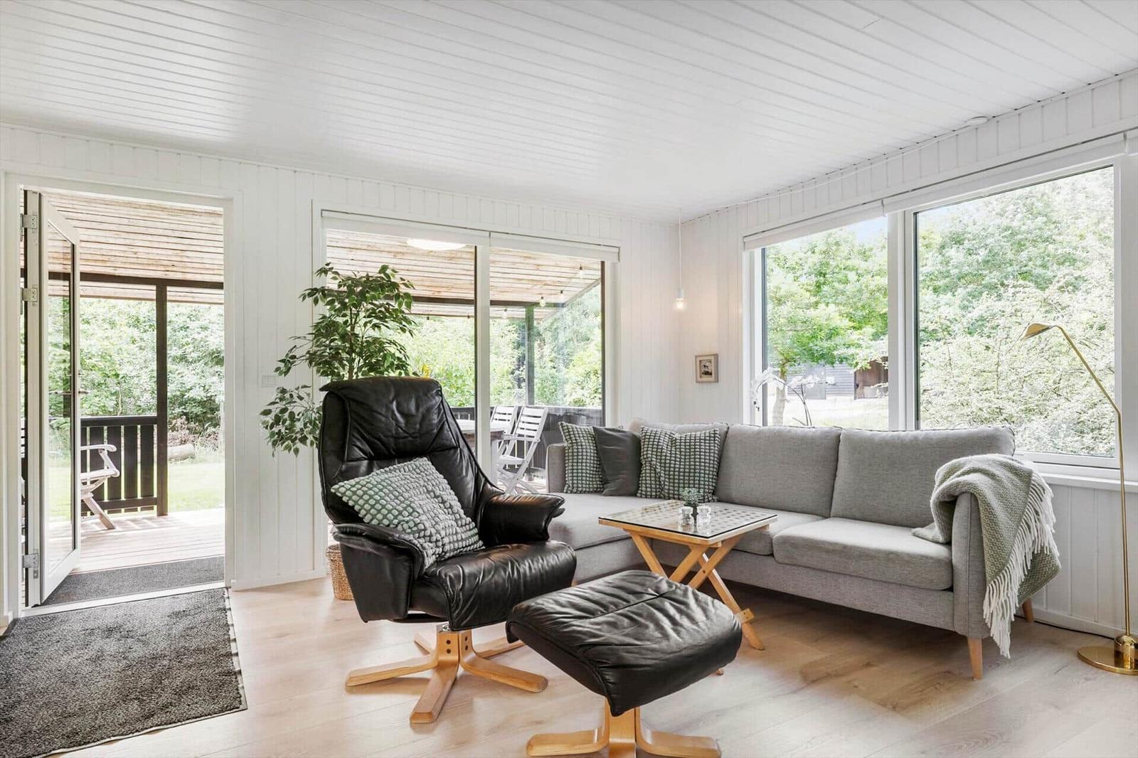 Wohnzimmer mit grauem Sofa, schwarzer Ledersessel und großem Fensterblick auf Garten.