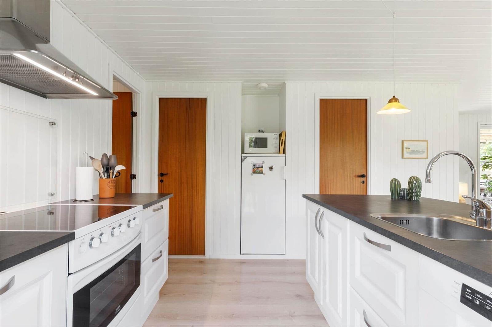Küche mit weißen Schränken, dunklem Arbeitsplatz und integriertem Kühlschrank.