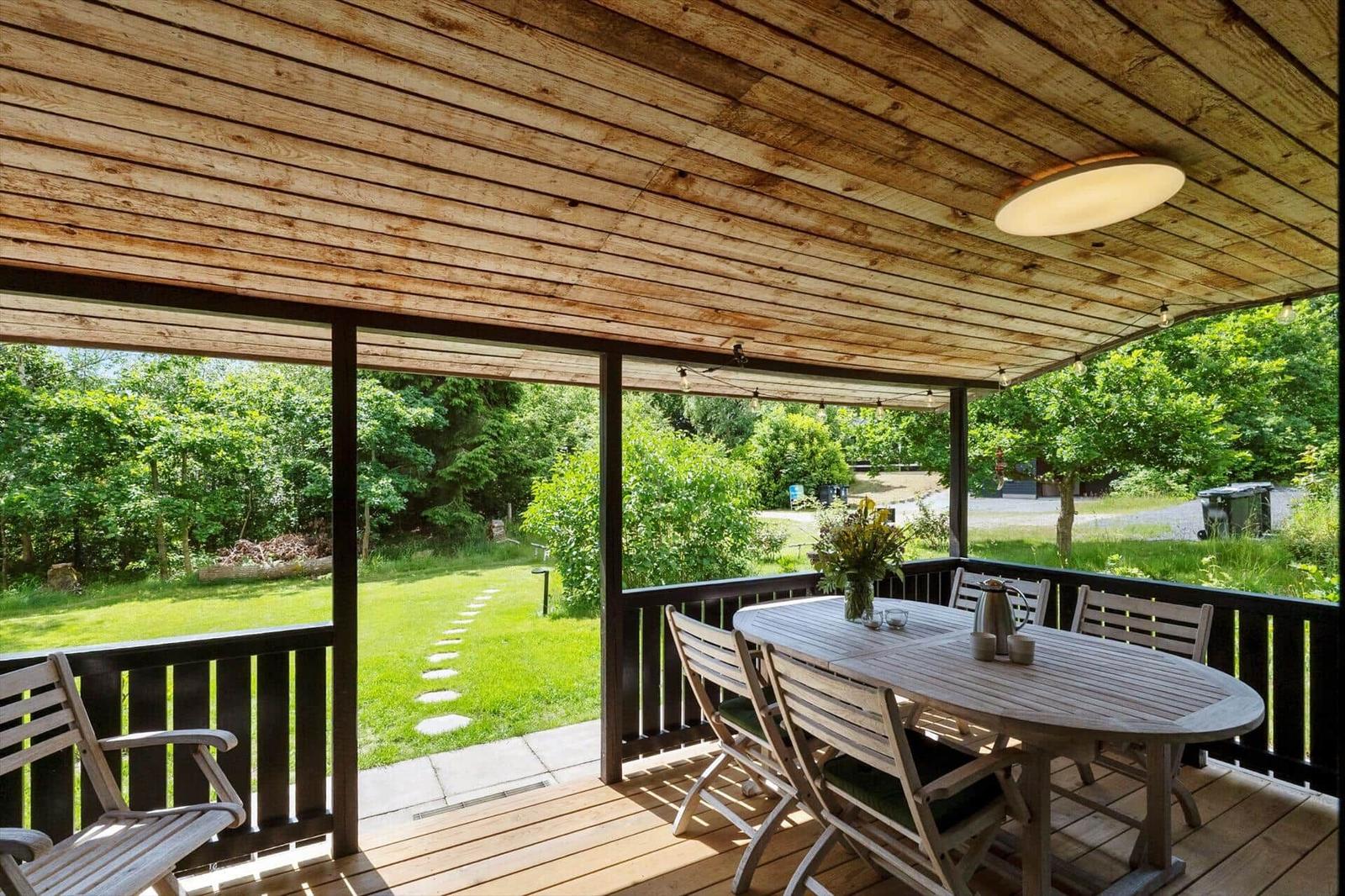 Terrasse mit Holzdecke, Tisch und Stühlen. Blick auf grünen Garten mit Weg.