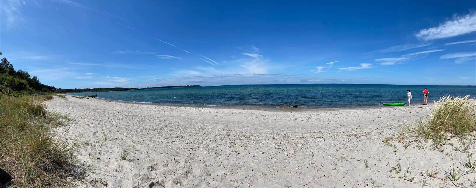Wide sandy beach promenade with clear sea and blue sky. Two people stand at the shore.