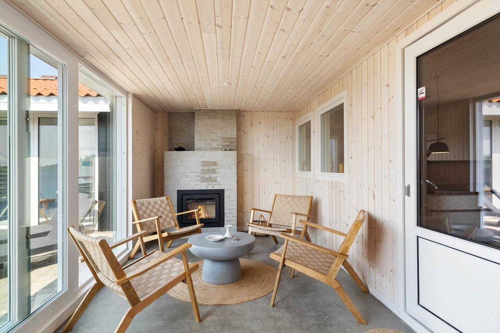 Terrasse mit Holzwänden, Kamin und vier Sitzgelegenheiten. Durchgehende Glasfronten.