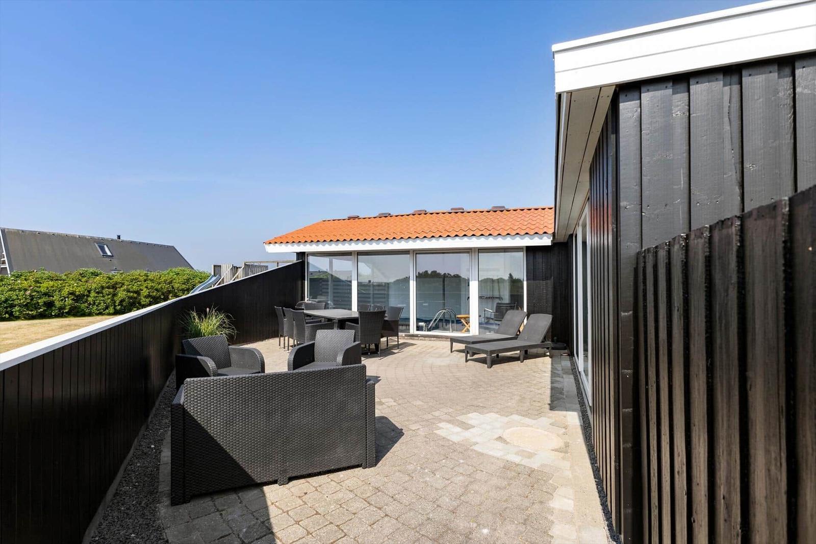 Terrasse mit Sitzgruppe, Liegen und Blick auf Poolbereich.