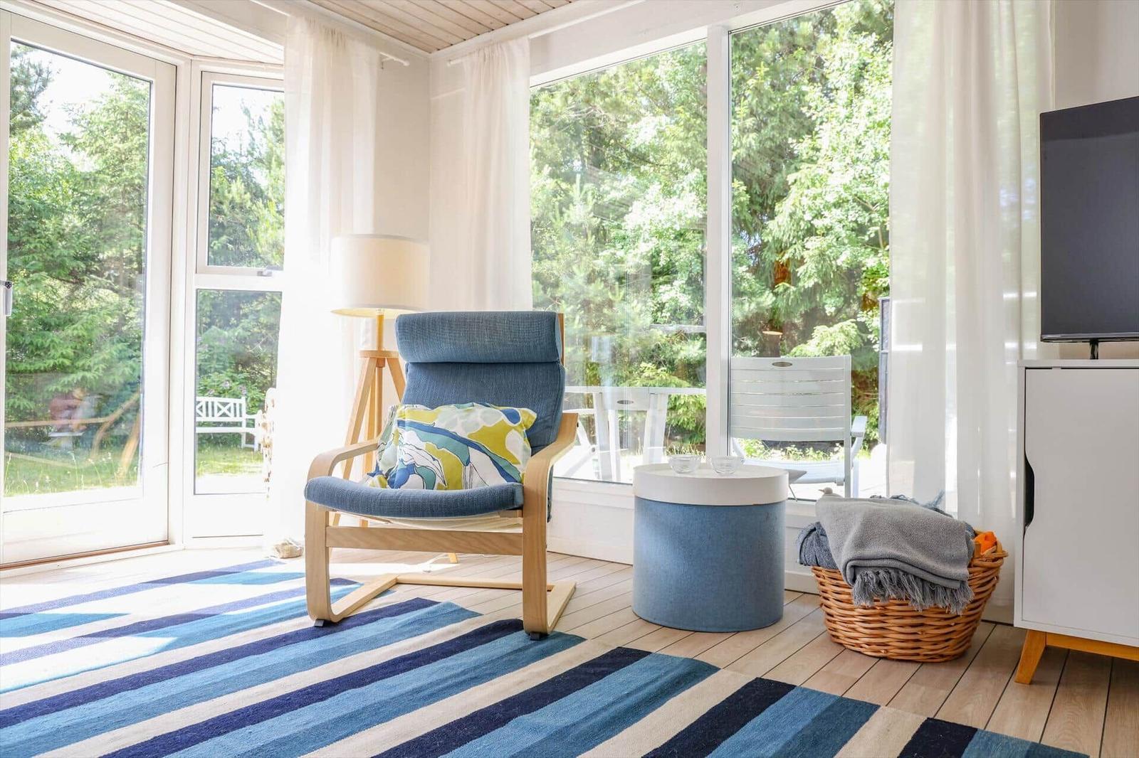 Ein Raum mit blauem Sessel, Streifen teppich und großen Fenstern zum Garten.