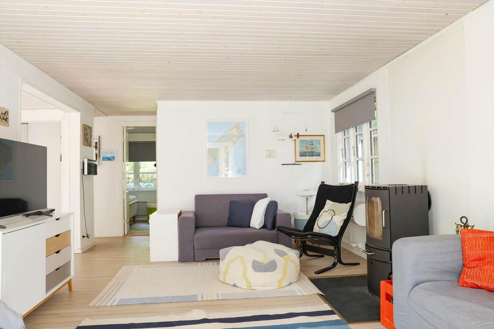 Wohnzimmer mit Sofa, Sessel und Kaminofen. Holzboden und weiße Wände.