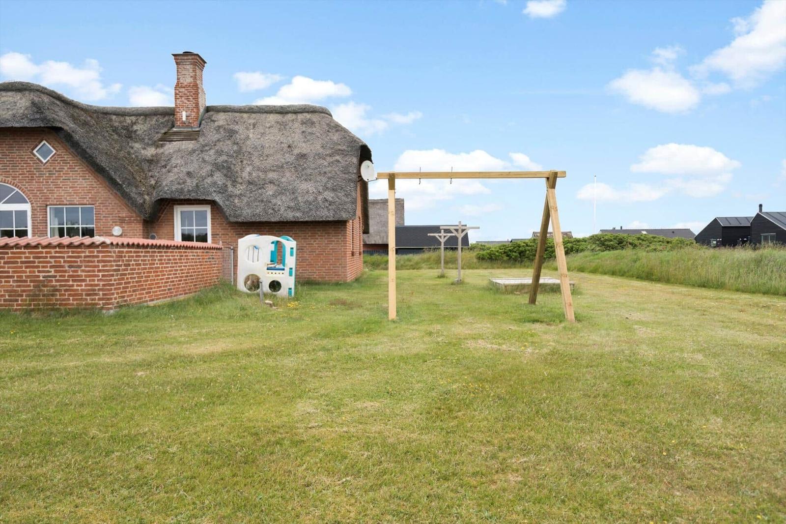 Haus mit Strohdach und Spielplatz im Garten.