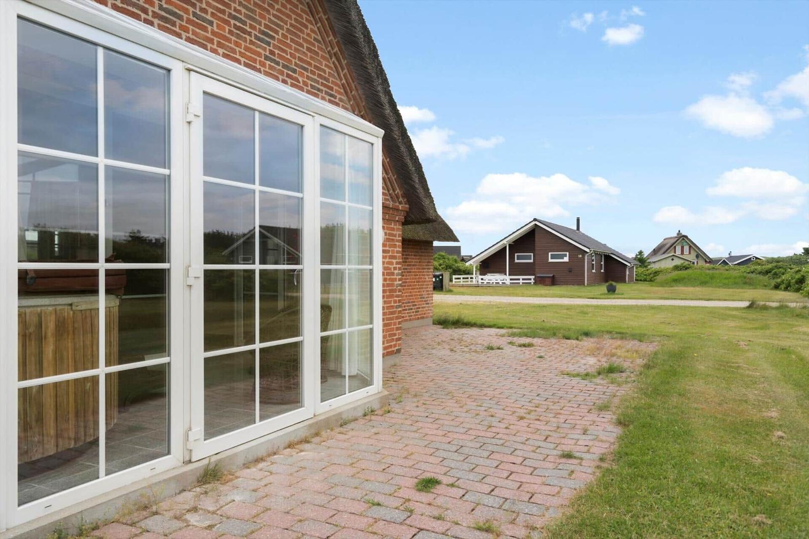 Haus mit großem Fenster, gepflasterter Hof und Blick auf grüne Landschaft.
