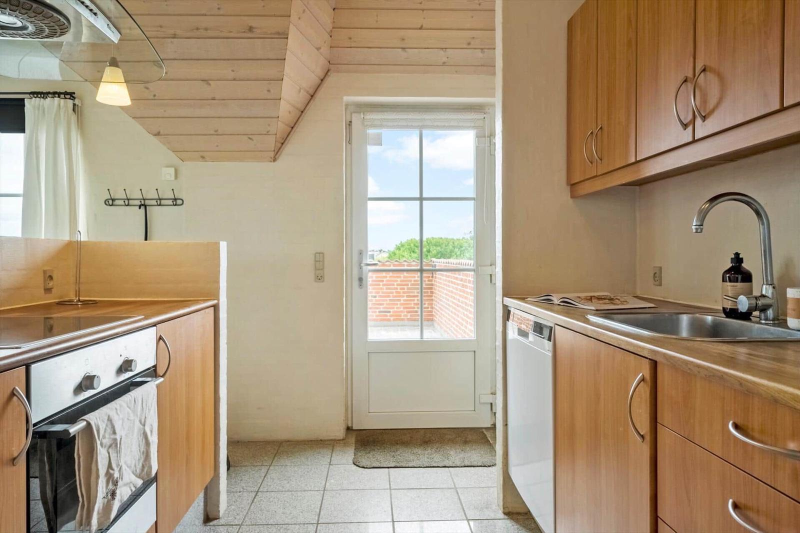 Küche mit Holzschränken, Spüle und Tür zum Balkon.