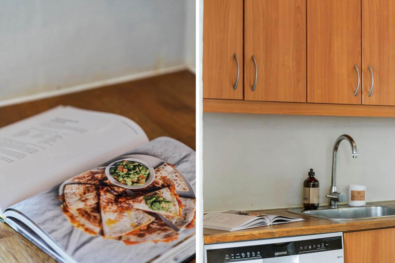 Küche mit Holzschränken, Spüle und Waschmaschine. Rezeptbuch mit Quesadillas auf Tisch.