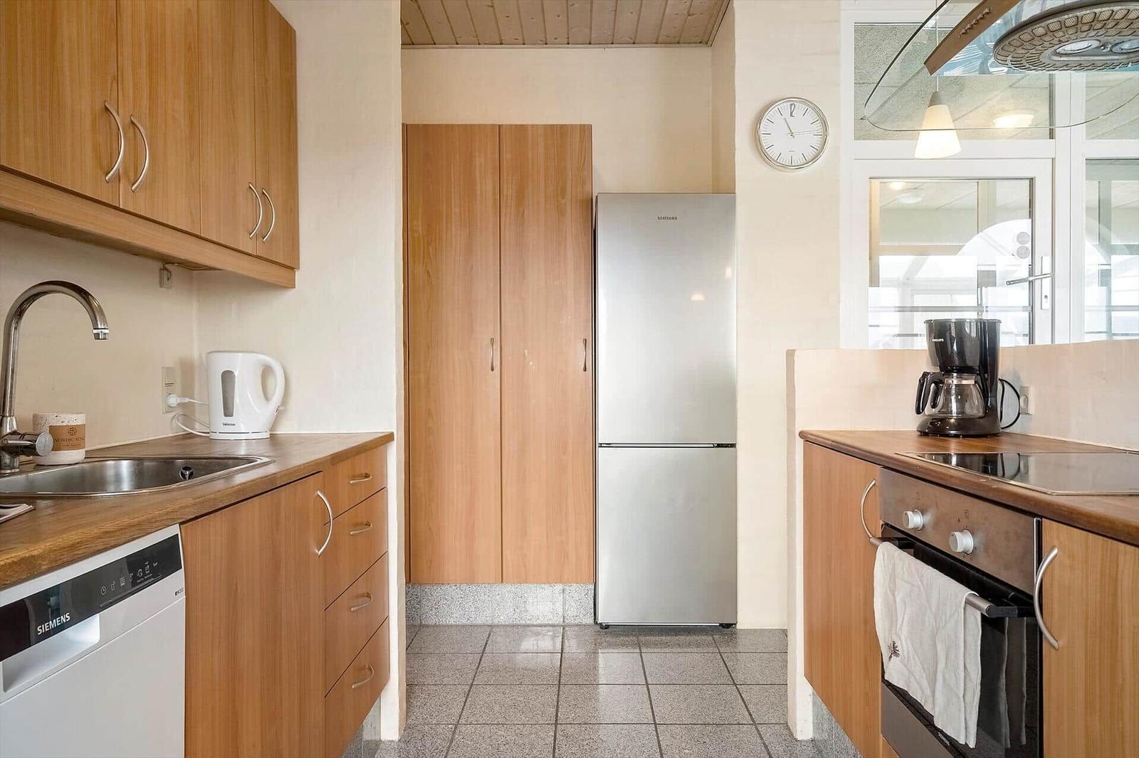 Küche mit Holzschränken, Kühlschrank, Spüle und Kochfeld.