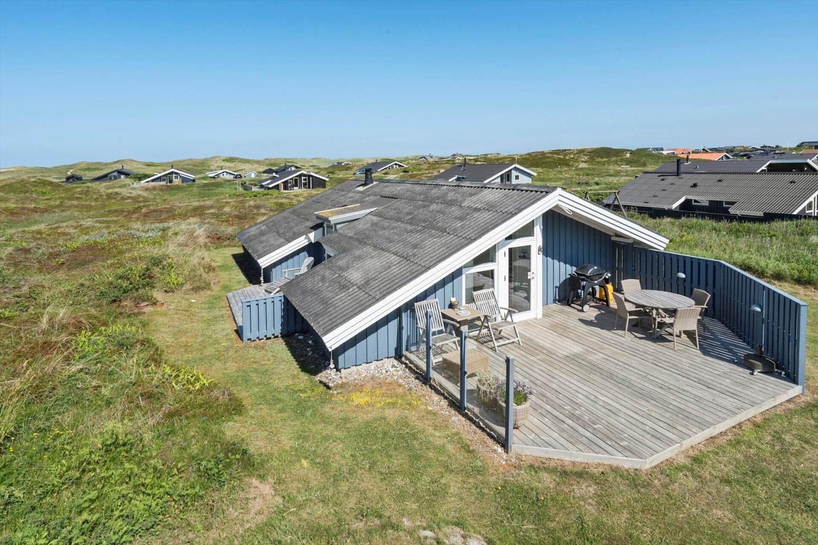 Moderne Strandhütte mit Terrasse, Grill und Garten. Blick auf Dünenlandschaft.