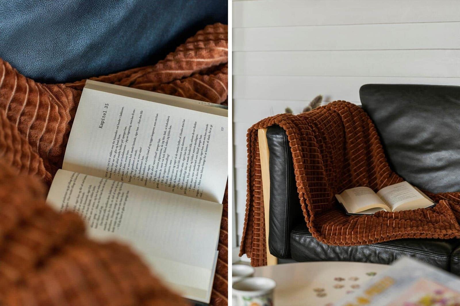 Ein schwarzes Sofa mit brauner Decke und einem offenen Buch.