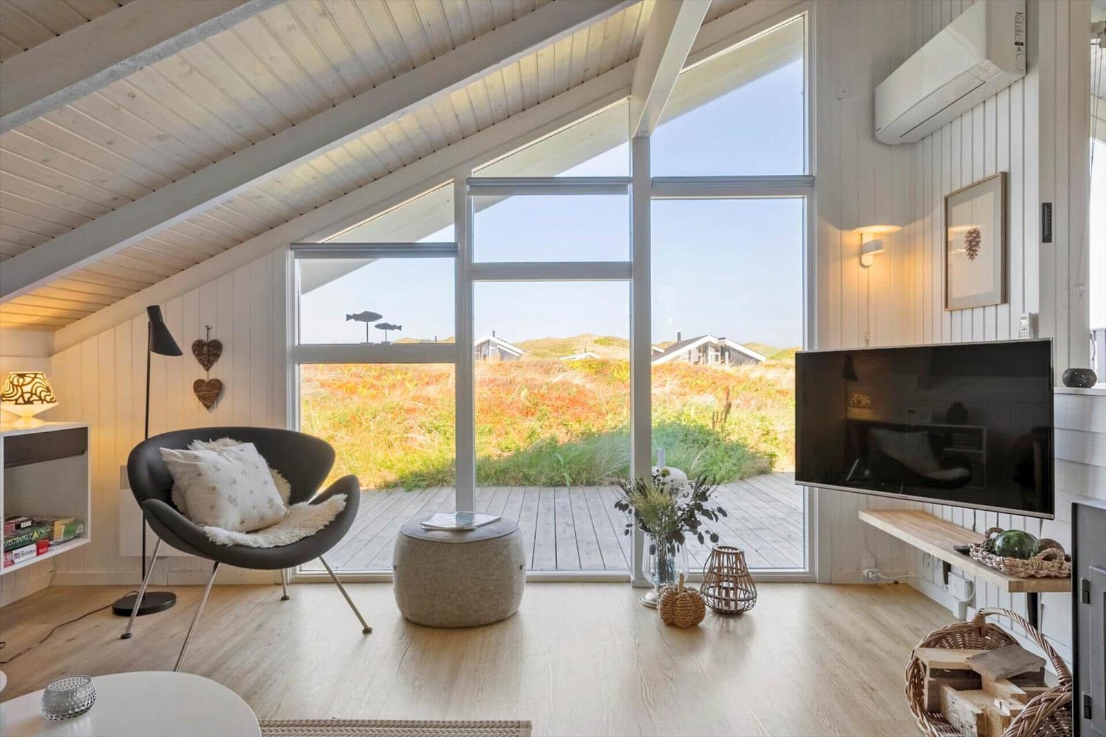 Wohnzimmer mit großem Fenster, Sitzgelegenheit und Fernseher. Holzboden und Dachschrägen.