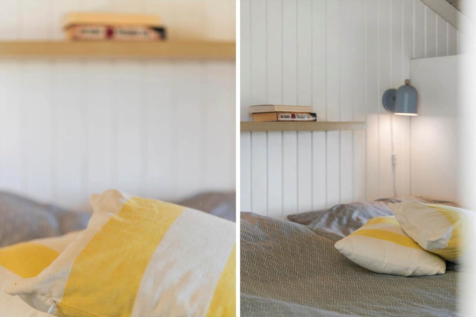 Schlafzimmer mit Bett, Kissen und Wandlampe. Holzregal mit Büchern an der Wand.