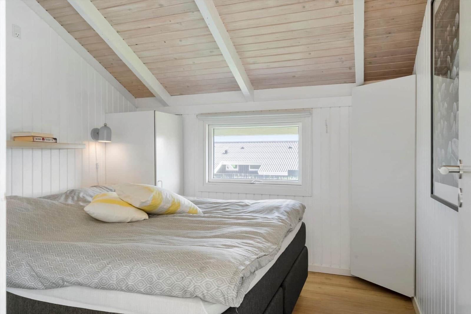 Schlafzimmer mit Bett, Fenster und Holzdecke.
