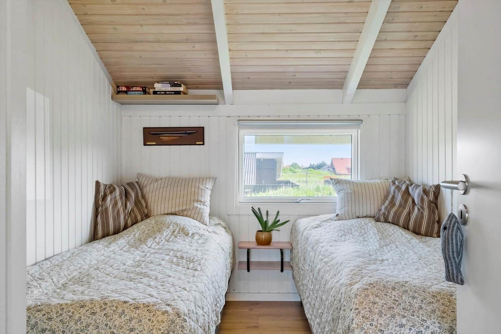 Zwei Betten mit Kissen und Decken, ein Fenster, eine Pflanze und ein Regal an der Wand.