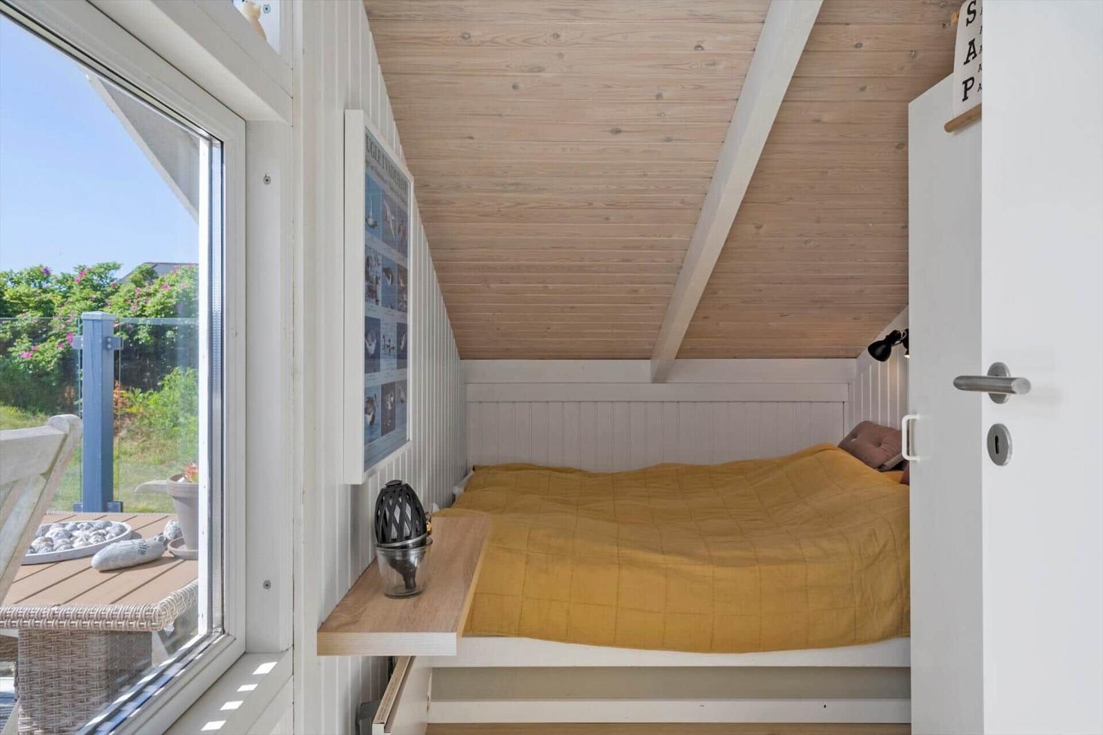 Schlafzimmer mit Bett, Holzdecke und großem Fenster zur Terrasse.