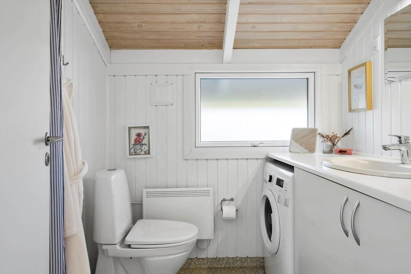 Badezimmer mit Toilette, Waschmaschine und Waschtisch unter Holzdecke.