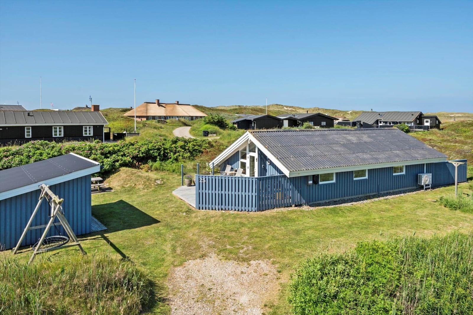 Blauer Holzhaus mit Terrasse und Garten. Umgeben von Gras und weiteren Häusern.