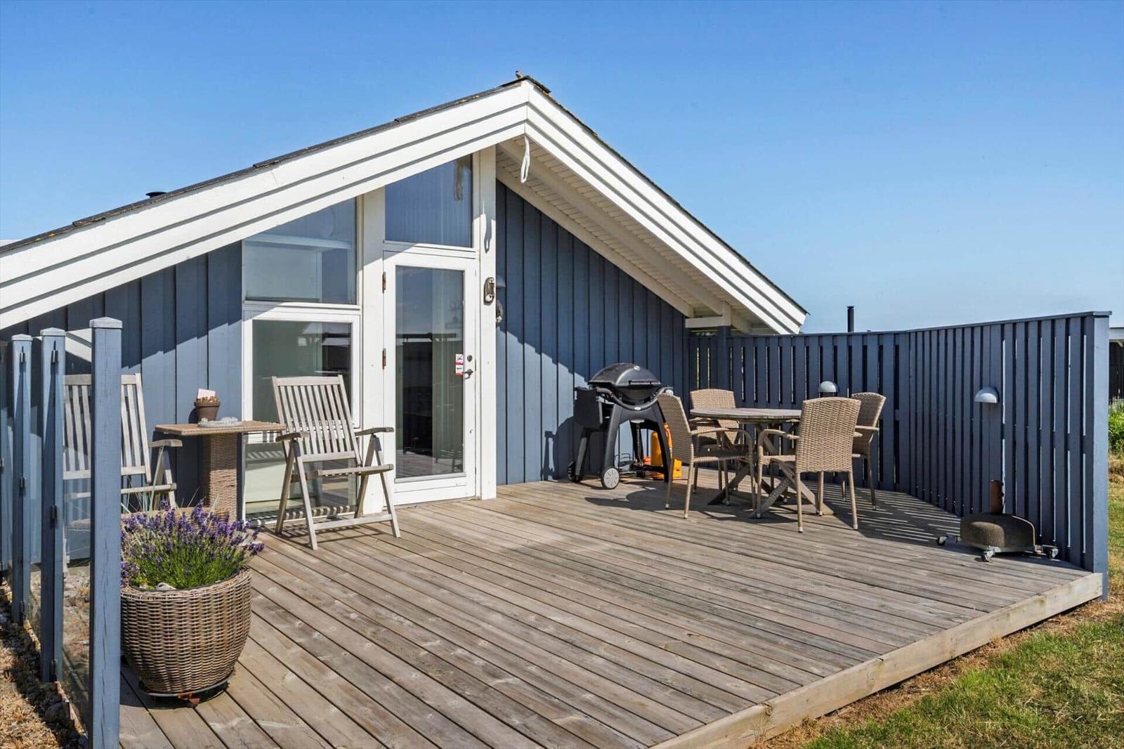 Terrasse mit Grill, Tisch, Stühlen und Pflanze vor einem Haus mit blauen Wänden.