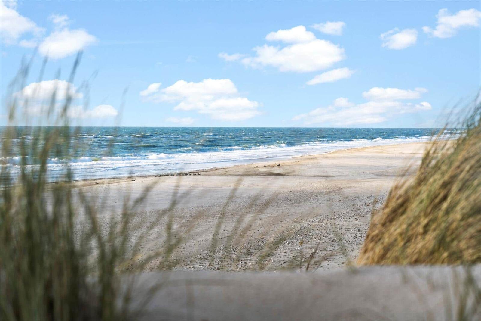 Strandblick mit Wellen, Sand und Dünengras im Vordergrund.
