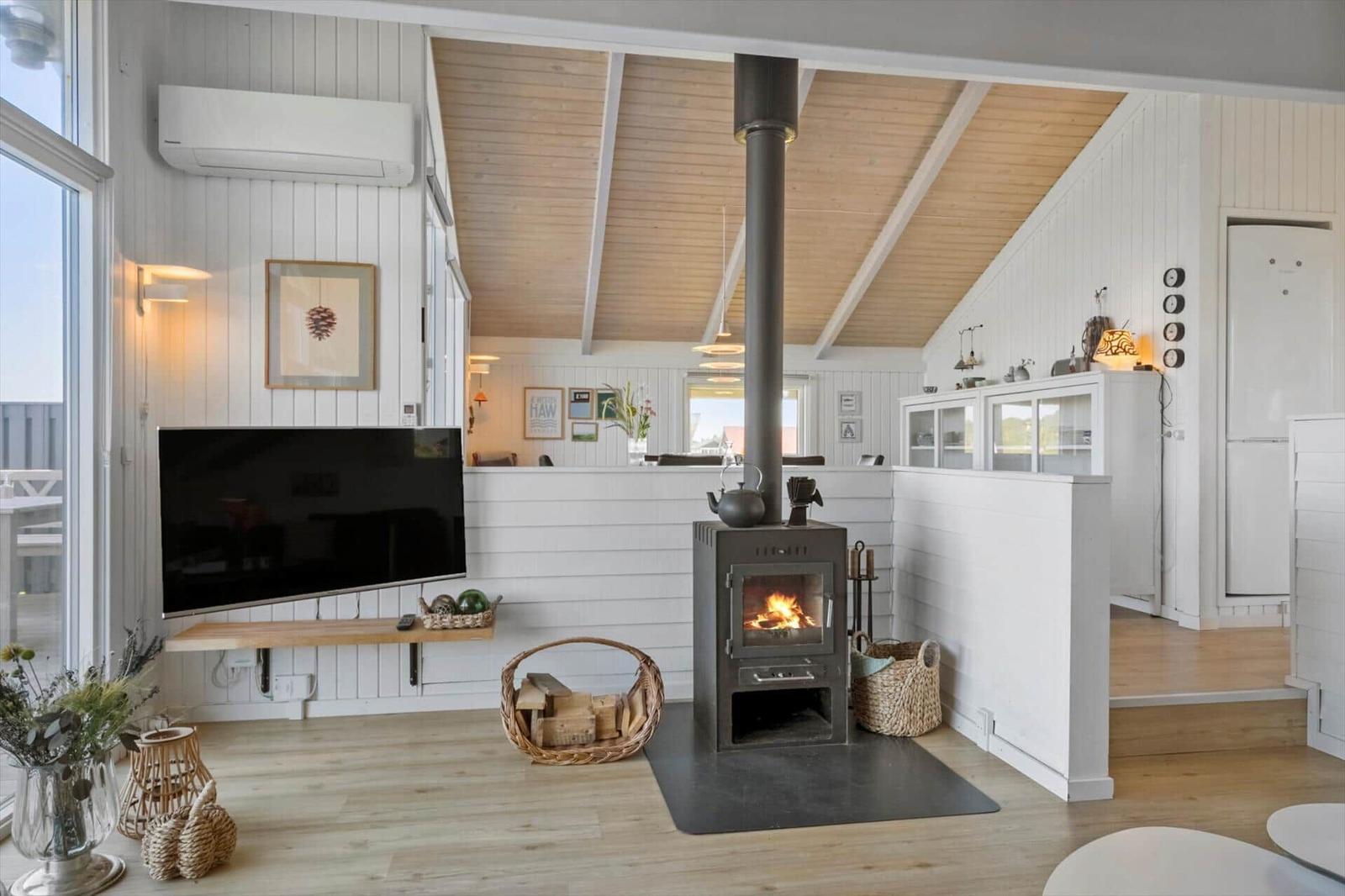 Wohnraum mit Kaminofen, Fernseher und Holzboden. Weiße Wände und Holzdecke.
