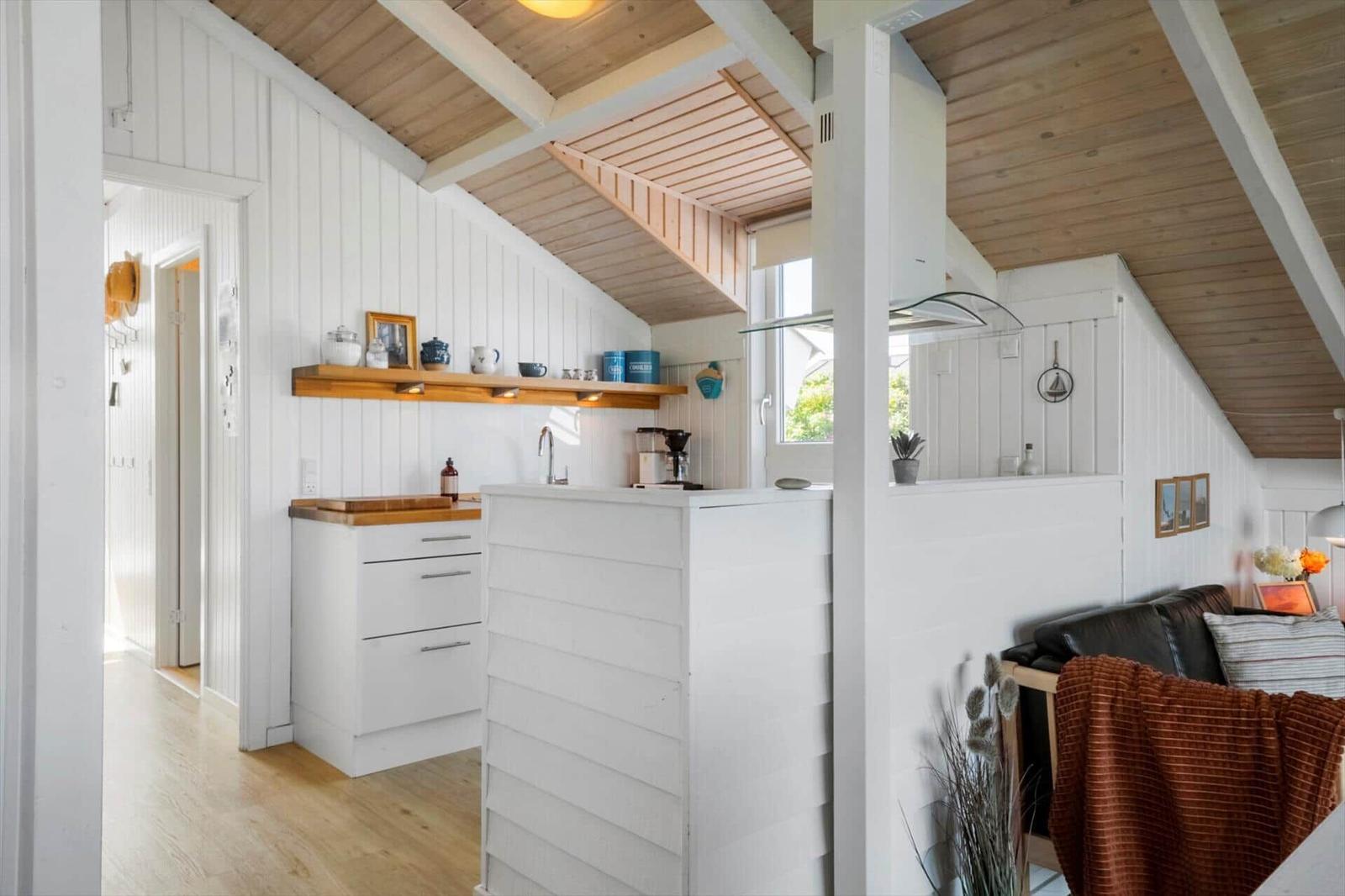 Küche mit Holzoberfläche und Wohnbereich unter schrägen Dachdecken mit weißen Wänden.