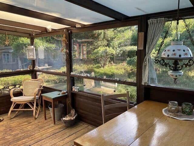 Glass roof with wooden floor, seating area and table. View of garden with trees.