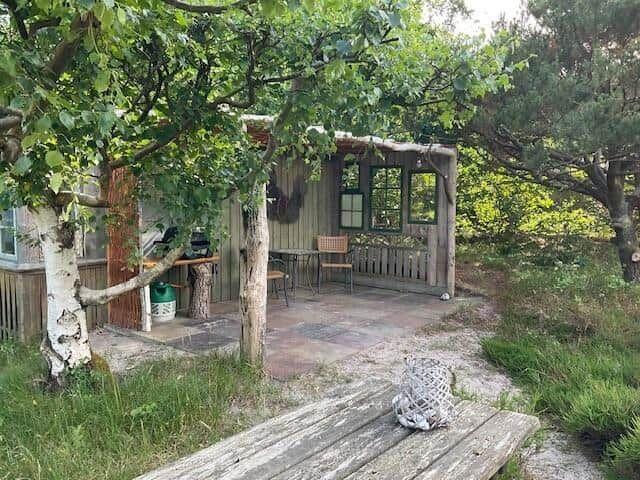 Cabin with terrace, table and chairs under trees. Wooden table in foreground.