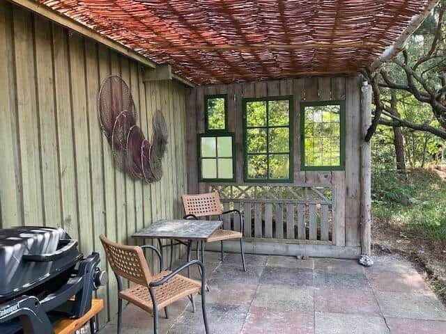 Patio with table, chairs, and grill under a thatched roof.