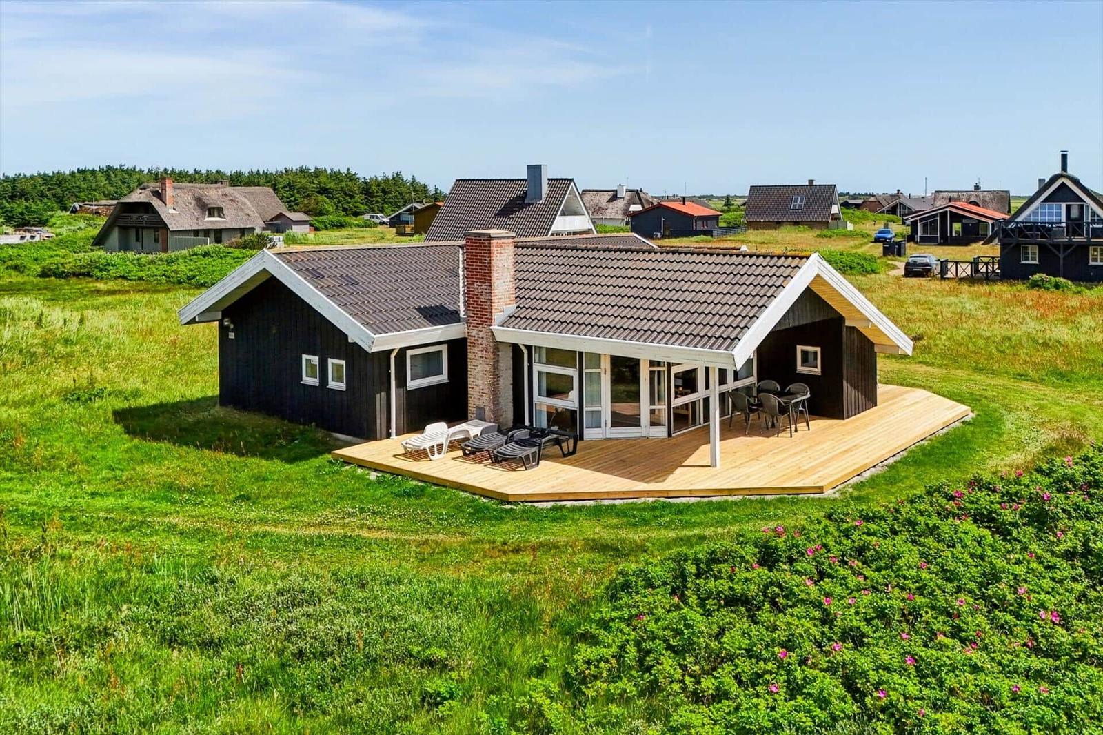 Moderne Ferienhaus mit Holzterrasse, Garten und Sicht auf die Umgebung.
