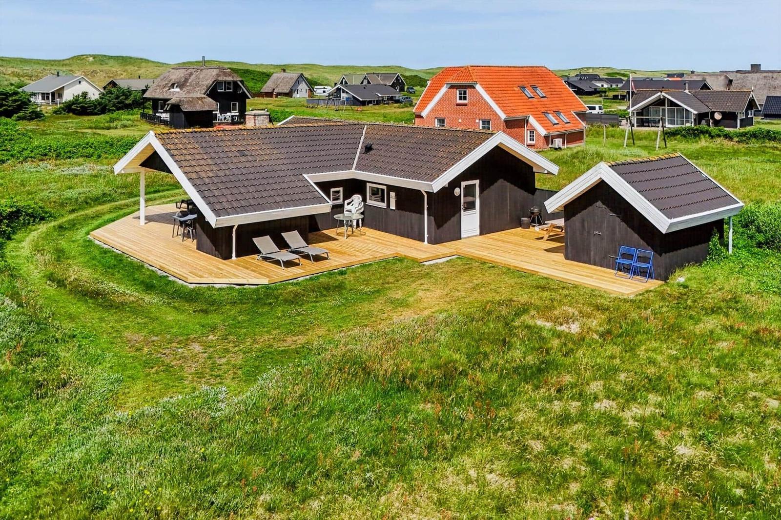 Holzhaus mit Terrasse und Grillplatz in grüner Landschaft.