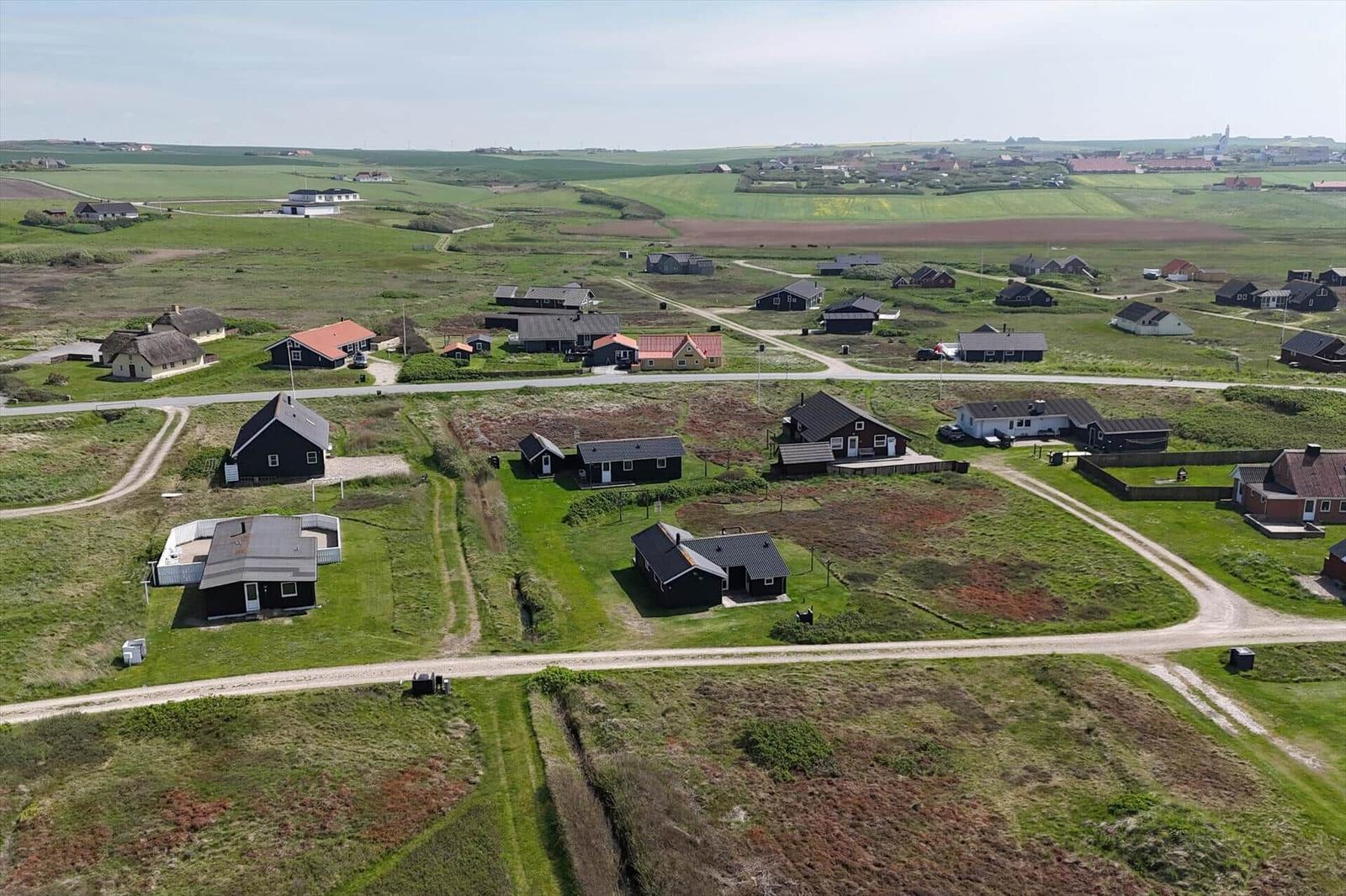 Aerial view of scattered houses on green fields with dirt roads.