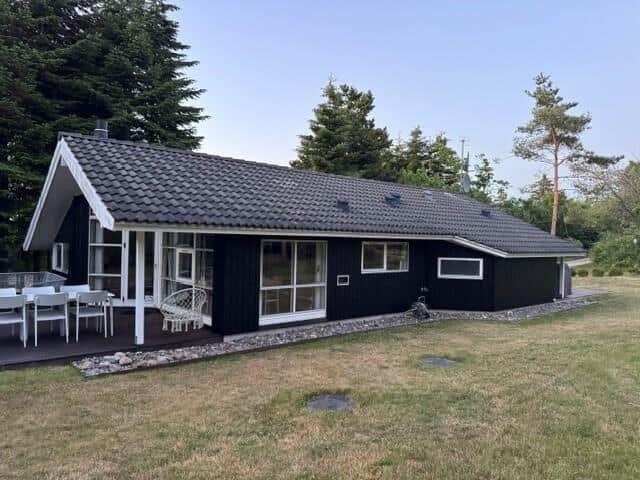 Black house with terrace, garden, and trees in the background.