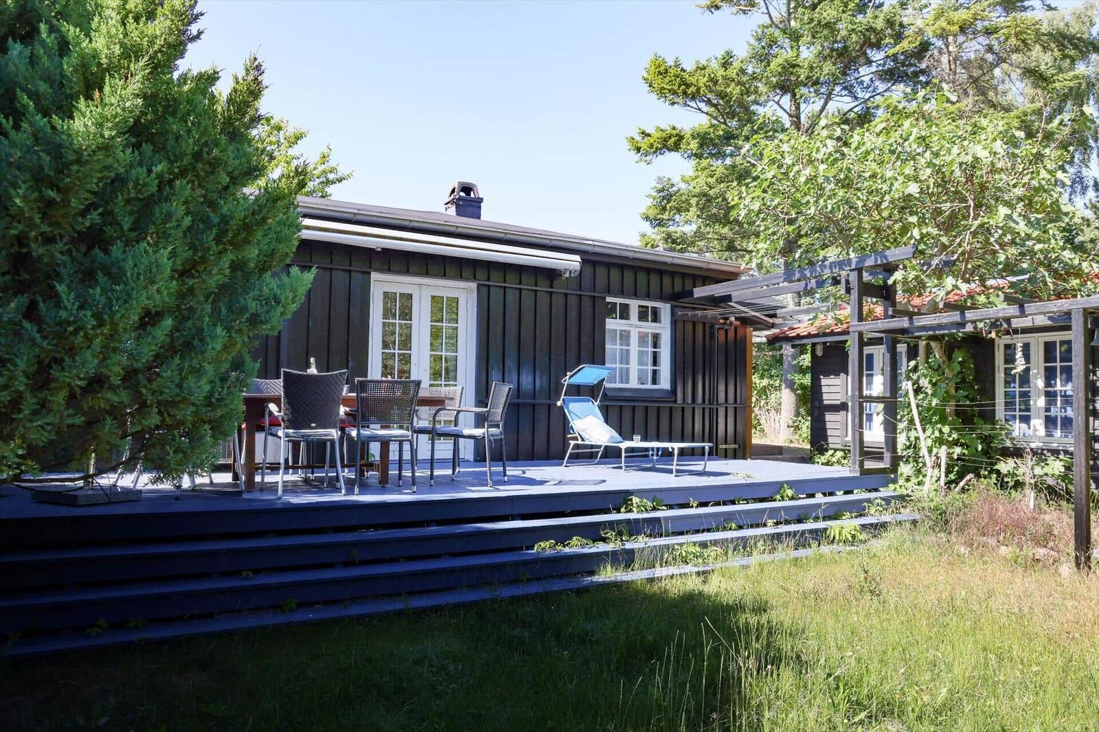 Black wooden house with terrace, garden, and sun lounger.
