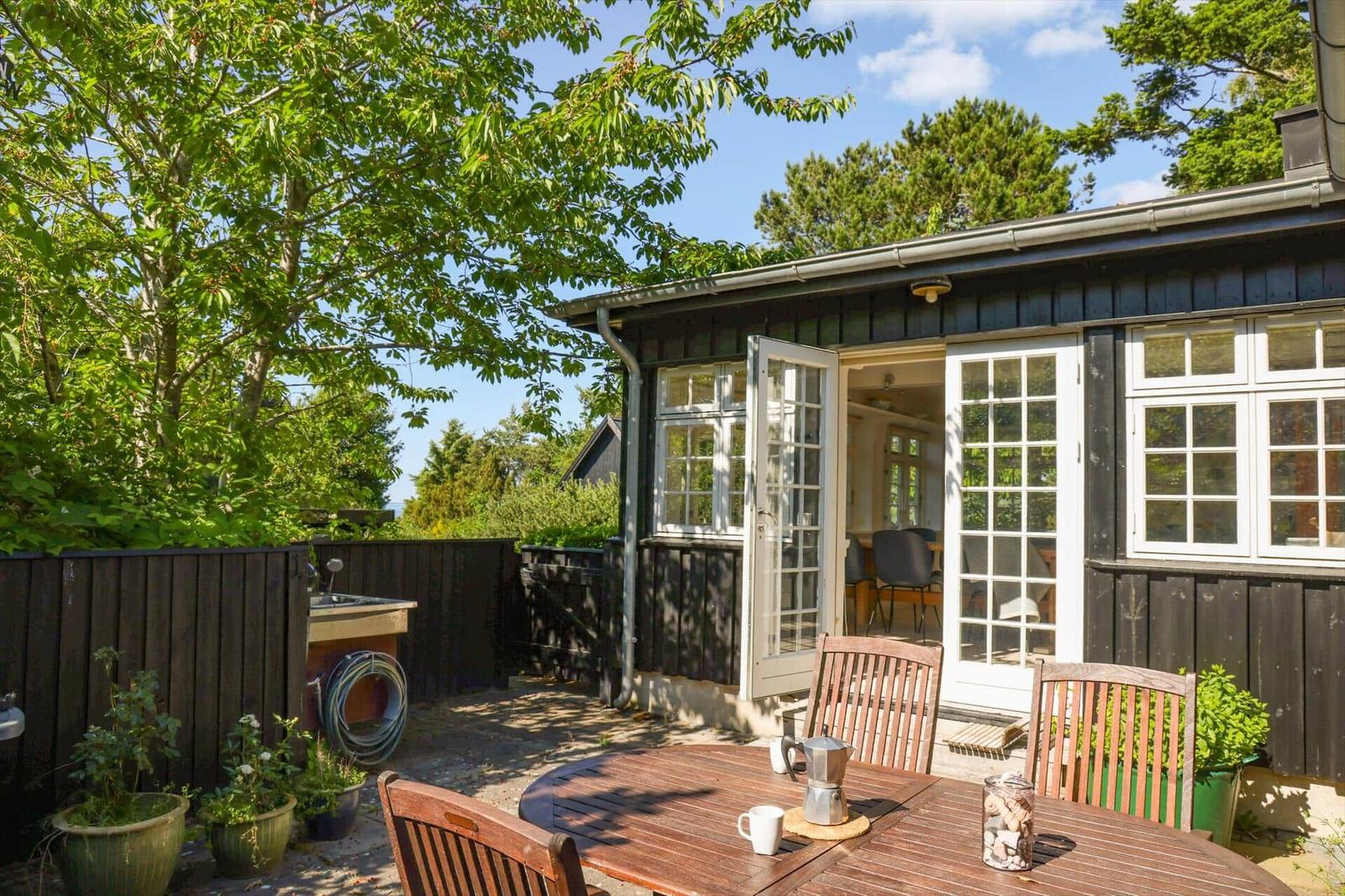 Terrace with table and chairs in front of a house with open windows.