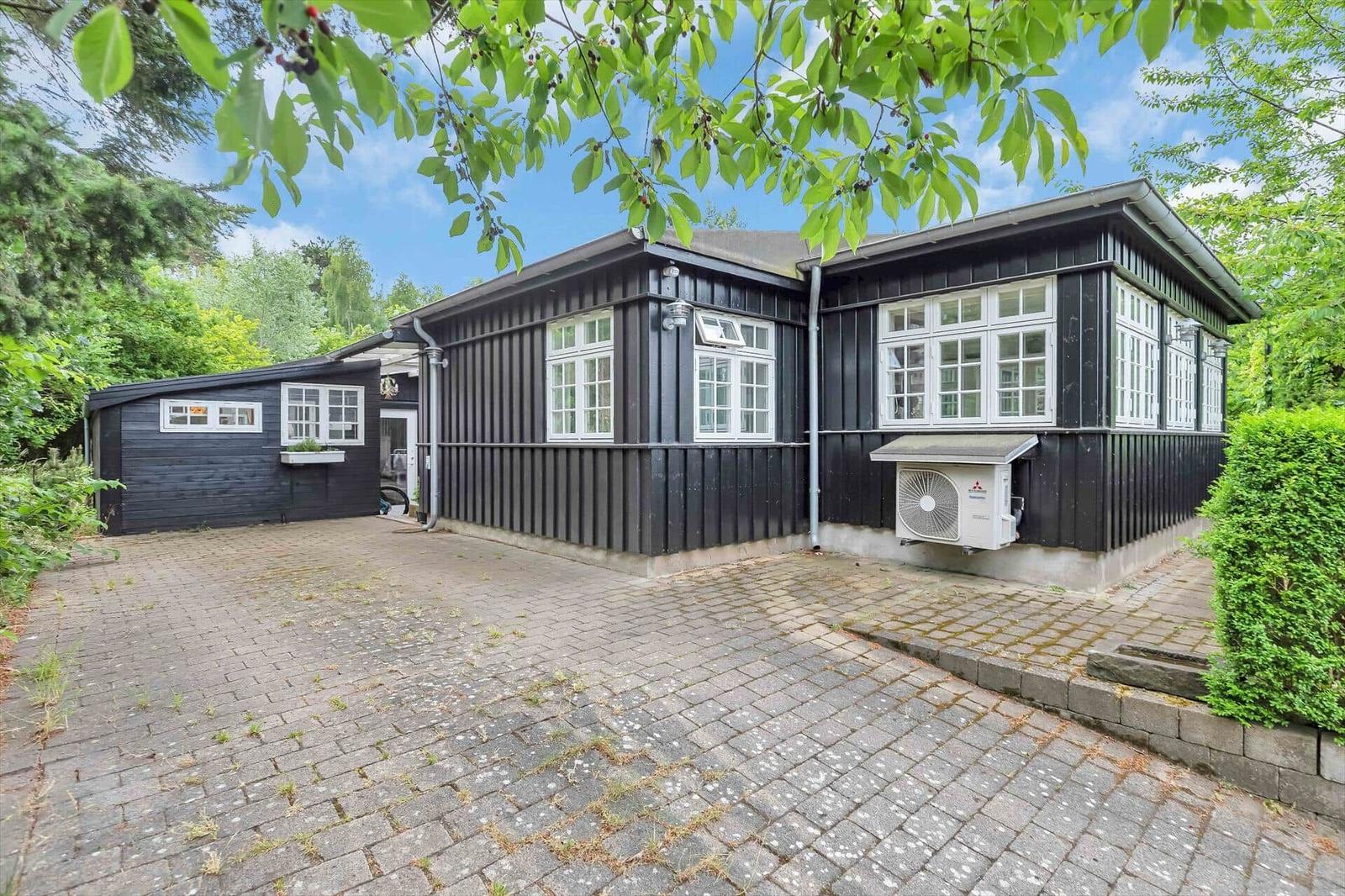Black wooden house with white windows and paved courtyard in greenery.